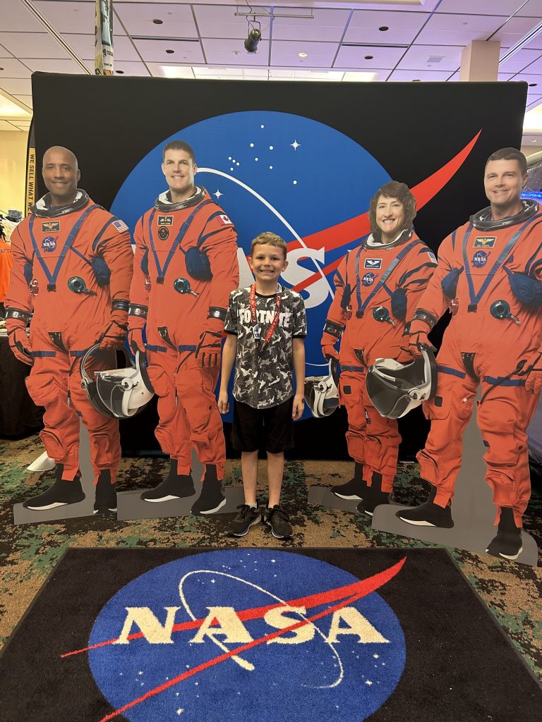 A young participant poses for a photo with life size cardboard cutouts of the Artemis II crew.