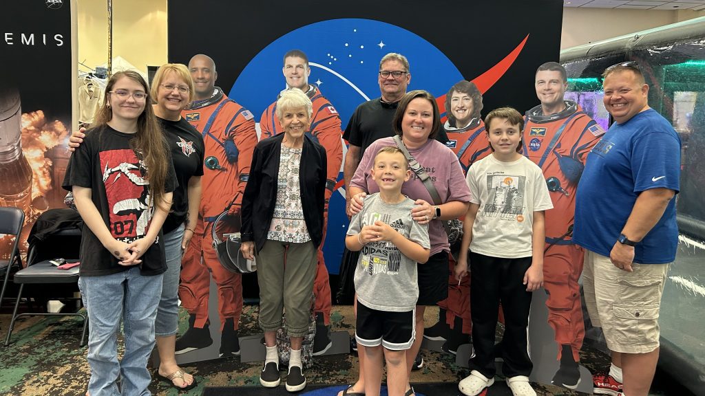 A family of participants pose for a photo with life size cardboard cutouts of the Artemis II crew.