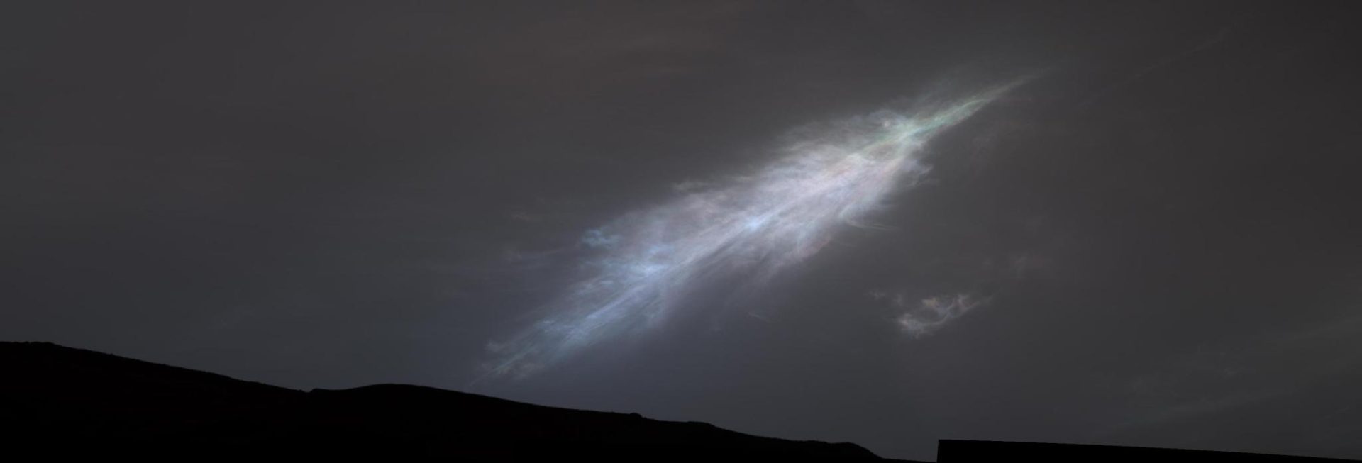 A shining, feather-shaped cloud in the dark gray Martian sky. The cloud is white, with a faint rainbow tint.